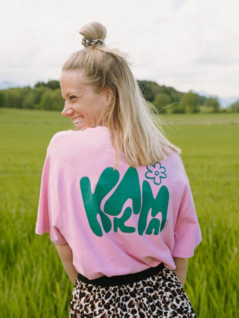Frau trägt das rosa KARMA Oversized T-Shirt mit großem grünem KARMA-Print auf dem Rücken, Größe M