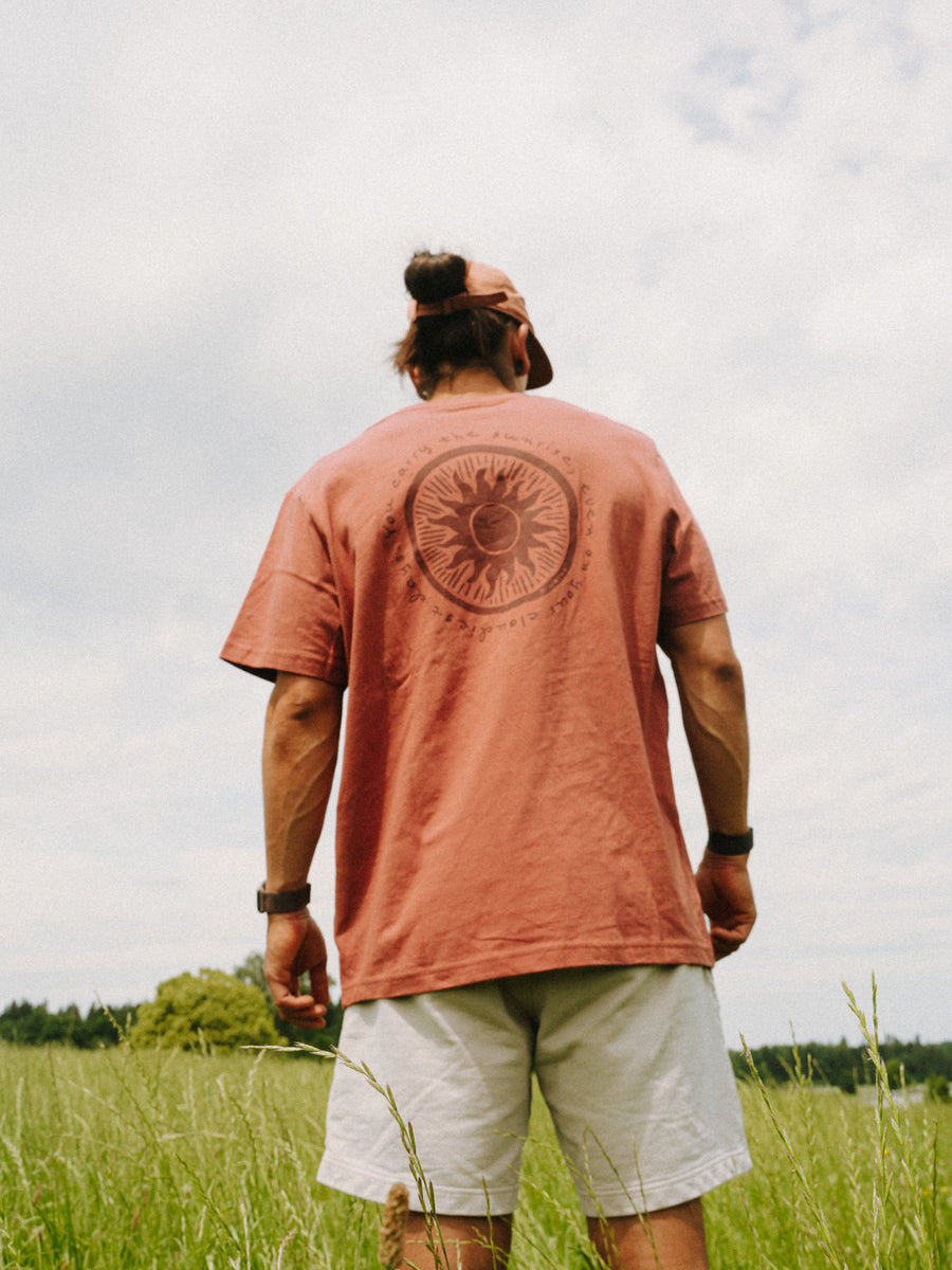 Mann trägt das SUNRISE T-Shirt in Rost von hinten – runder Sonnen-Print Ton in Ton auf dem Rücken, handbedruckt im Siebdruck